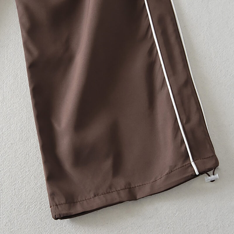 Close-up of brown oversized baggy high-waisted sweatpants with white stripe, made of breathable woven polyester fabric.